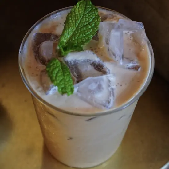 A close up of a milky iced coffee drink with mint sprigs on top.