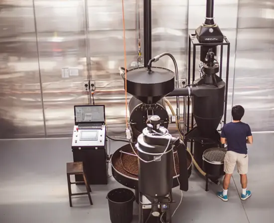 A man stands next to a large black roaster and air purifier.