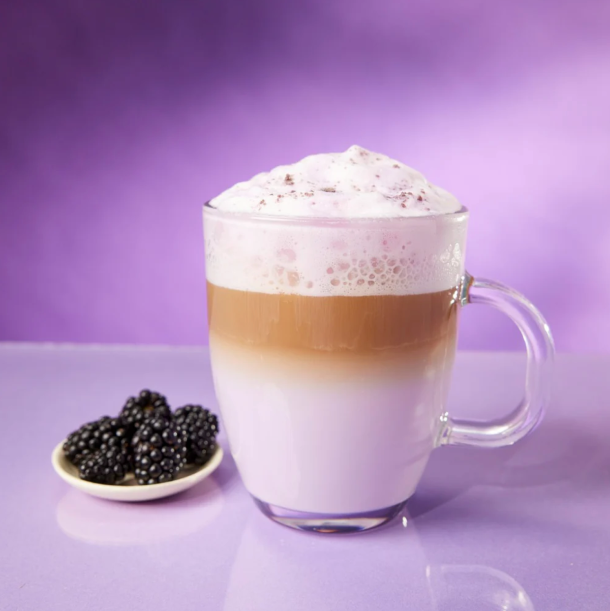 A Berry Bliss latte in a glass much with boysenberries on a dish next to it.