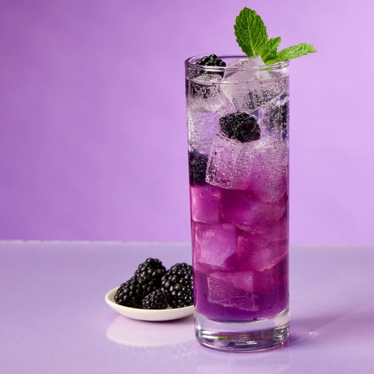 A Boysenberry Bramble in a tall glass with a small dish of boysenberries next to it.