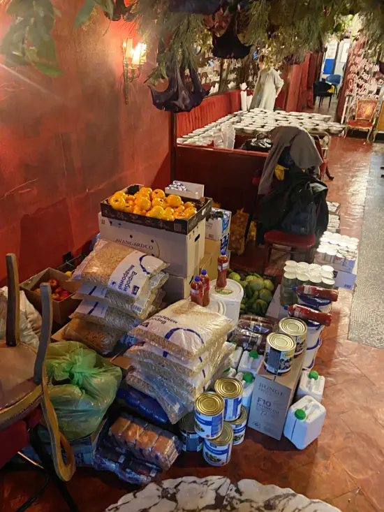 A stack of food and provisions are lined up against a wall: rice, canned goods, produce, etc.
