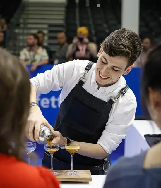 Daniele Ricci wears an apron and pours into cocktail glasses during the World Barista Championship in Athens, Greece.