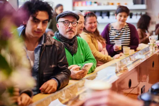 A line of people sit at the long wooden bar.