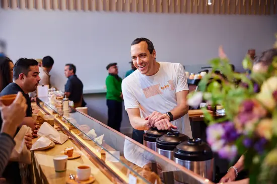 Luigi leans over coffee pots behind the espresso bar and talks to guests seated at the bar.