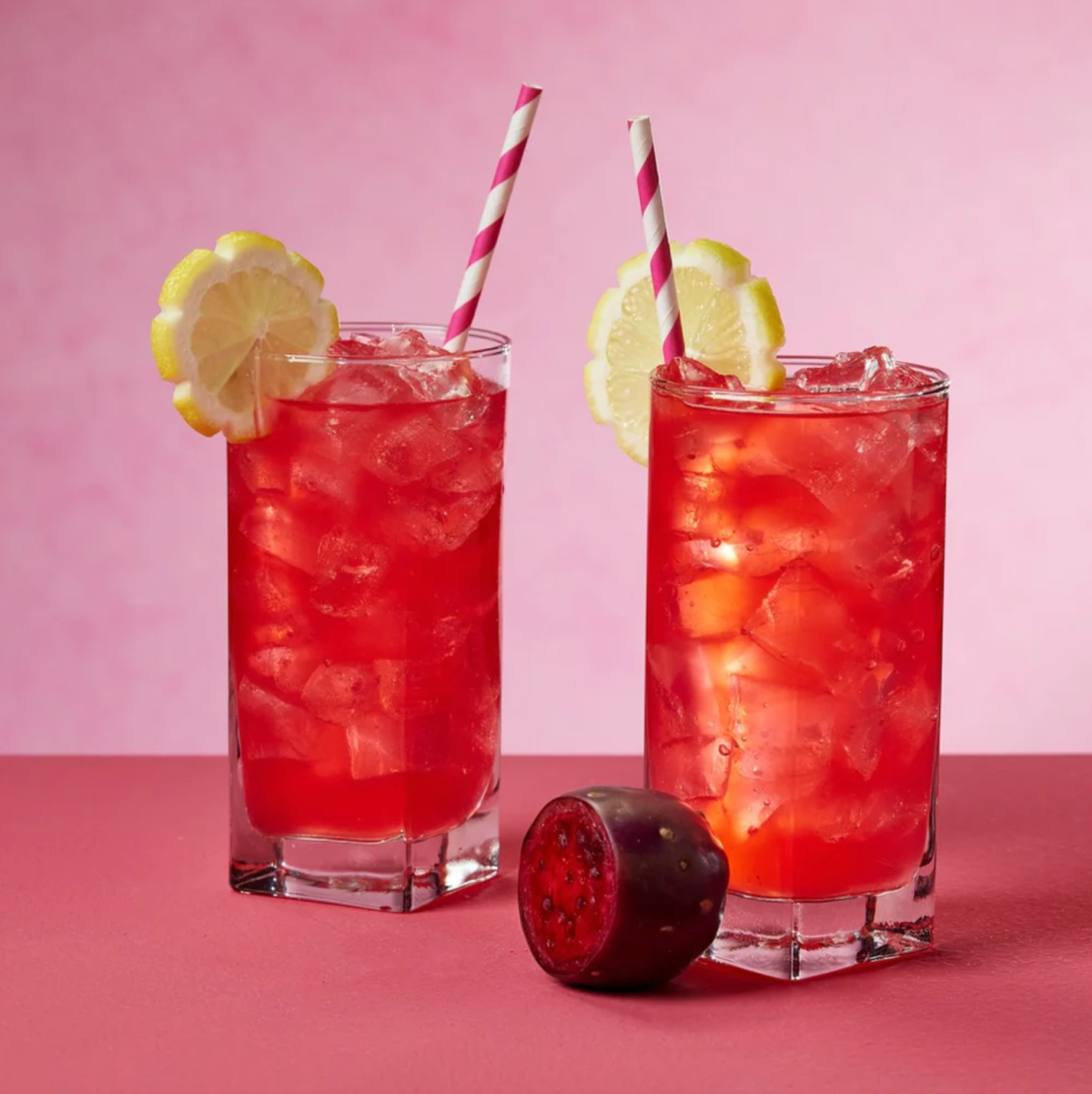 Two tall glasses of Prickly Pear Lemonade with a sliced prickly pear between them.