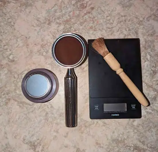 The portafilter, water cup, and a scale and brush set on a countertop.