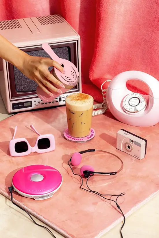 A shaken cold coffee drink with a hand hovering over it with a bartender's filter and surrounded by randome pink objects.