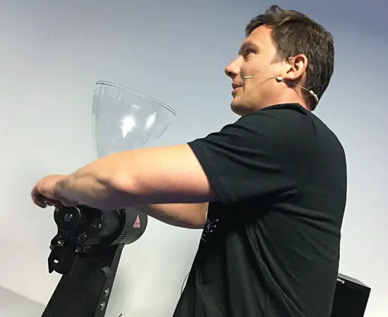 A man with microphone headset stands beside a coffee grinder.