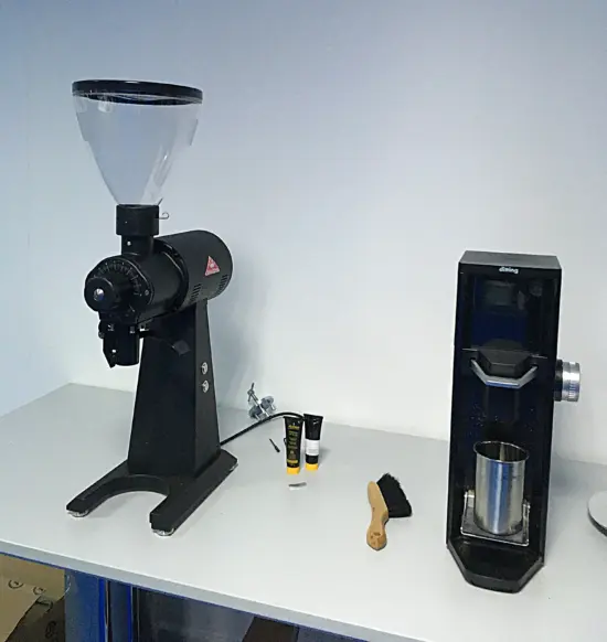 Two coffee grinders on a table with a cleaning brush.