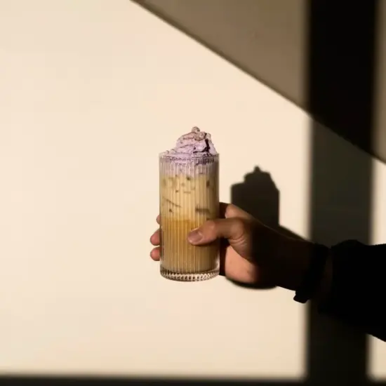 Hand holding an iced drink with purple whip.