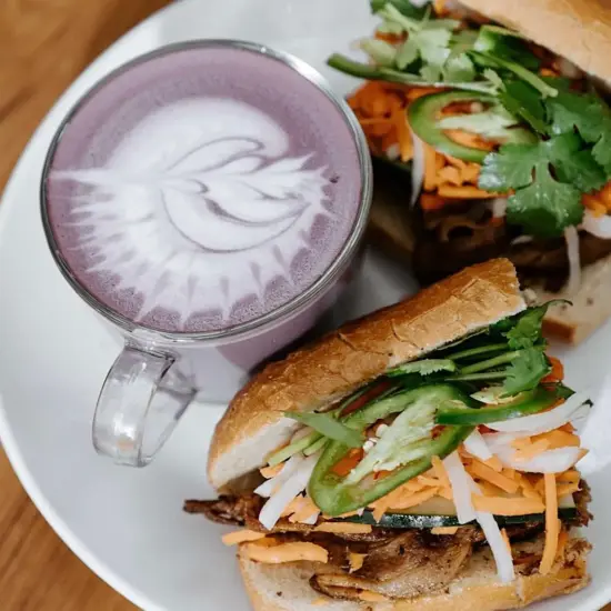 A hot purple drink next to a banh mi sandwich.