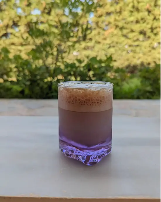 A clear purple glass with a shaken iced coffee beverage.