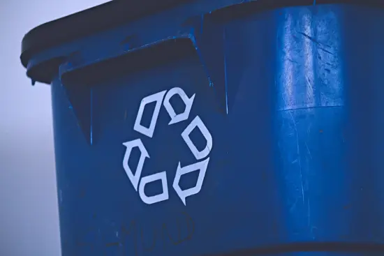 A close up of a blue recycling bin with a white recycling symbol on the front.