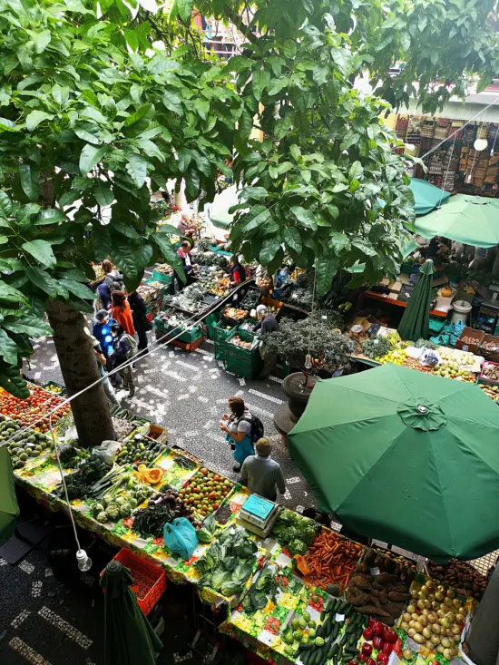 A bird's eye view of an outdoor farmer's market with tables of produce and green umbrellas.