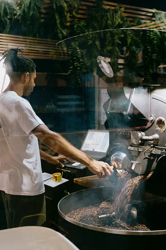 A man is roasting coffee beans on a large roaster behind glass.