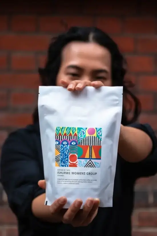 A person holds out a white bag of Burundi coffee from the Ishurwe Womens Group.