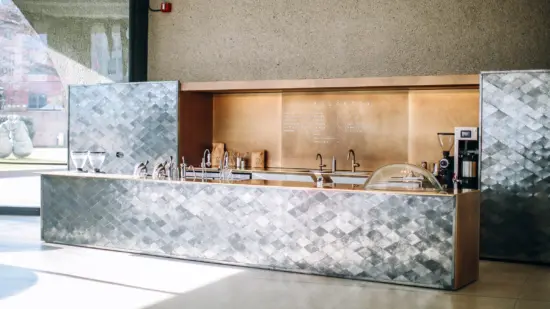 The coffee bar inside a museum features a silver front with a diamond fish scale pattern.