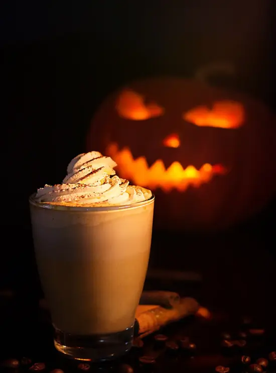 A beverage topped with whipped cream, with a jack-o-lantern in the background.