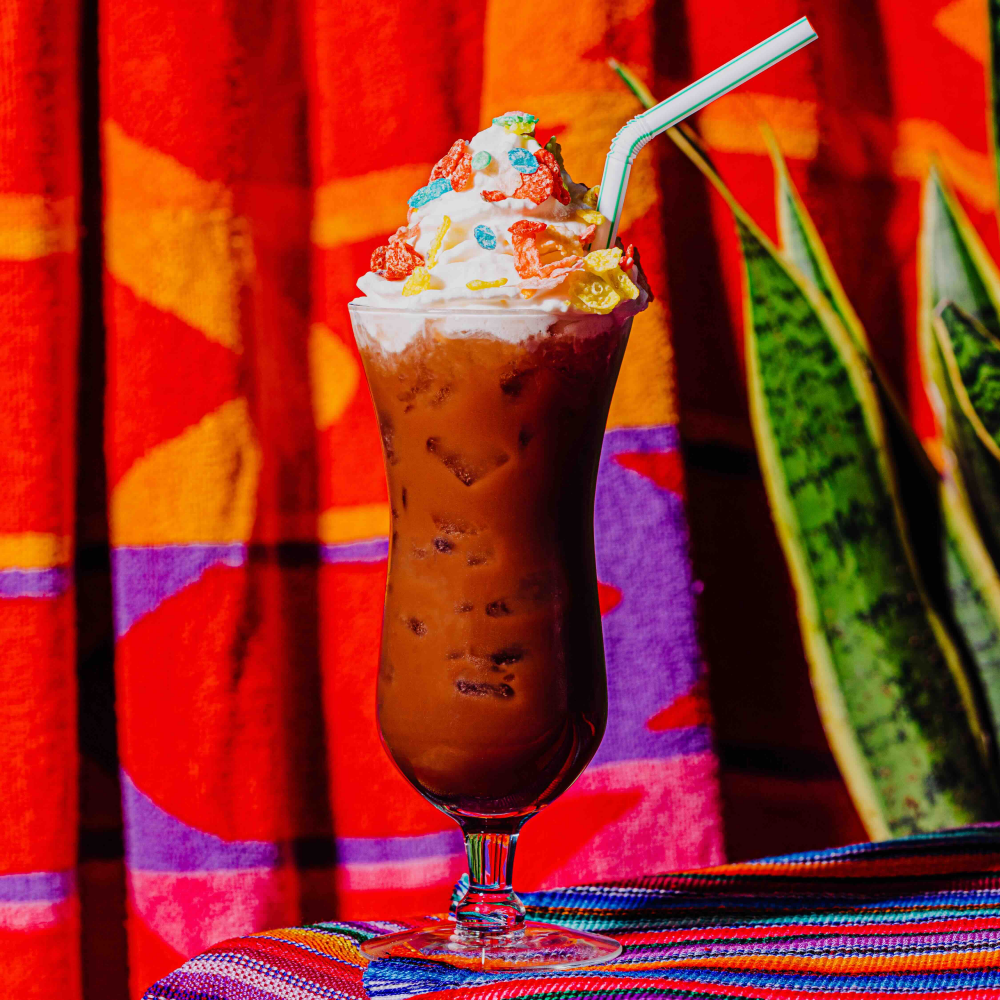 The Alegria ca. 1998 hot cocoa in a tall glass with a straw topped with whipped cream.