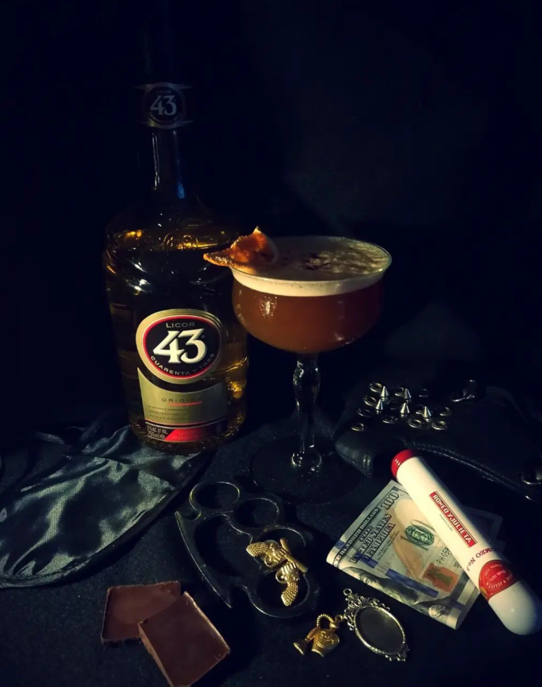 The winning drink in a glass topped with foam next to a bottle of Licor 43.