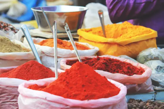 Bags of filled spices sit on a table, with large dipping spoons stuck into the spices.