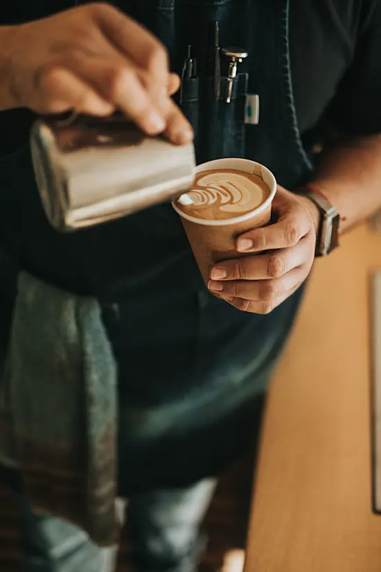 A barista pours a latte into a paper cup.