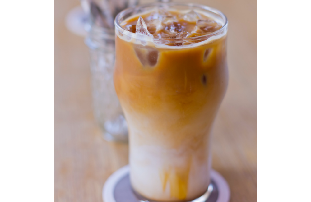 A honey spice almond cold brew latte in a tall glass with ice.