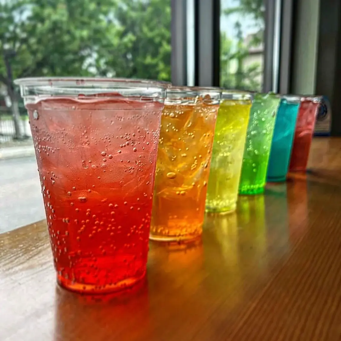 Six bubbly drinks lined up, all different colors from red to purple.