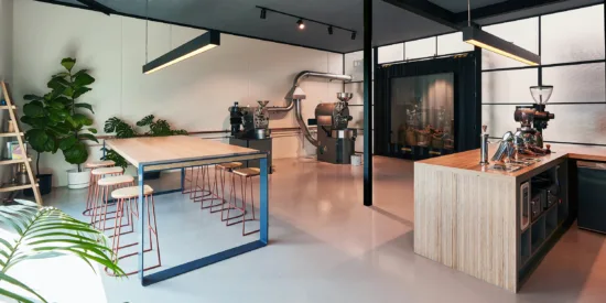 Inside of co-roasting space, with table and stools, coffee brewing counters, storage area and two roasters.