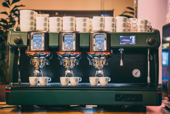 A green espresso machine with three groupheads and touchscreens.