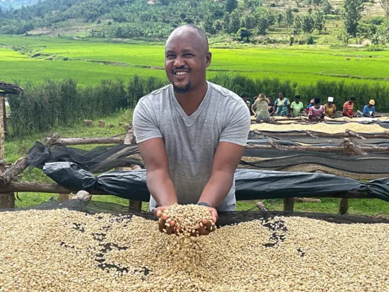 Eric holds green beans in his hands on a coffee farm with other workers in the background.