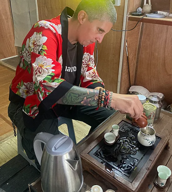The author wears a red kimono-like top and pours tea for the ceremony.