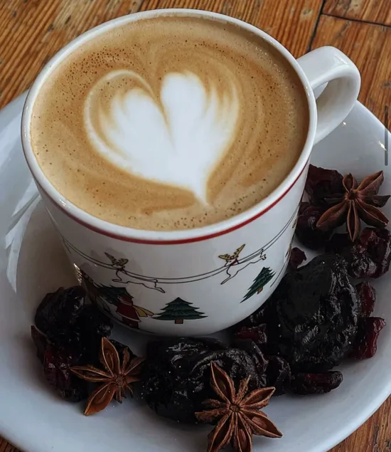 a Christmas them mug with a latte inside, and star anise and dried cranberries on the cup's saucer.