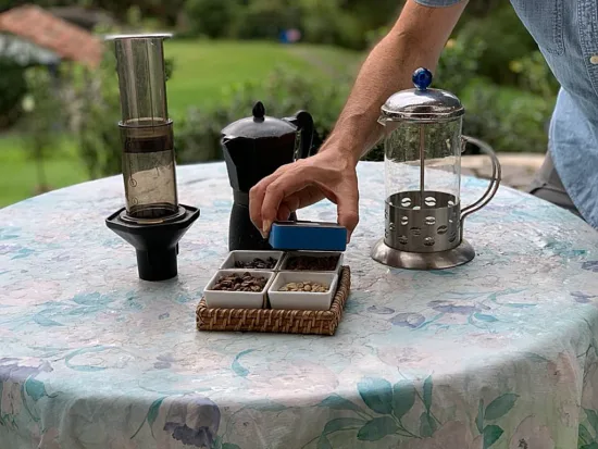 A small blue box, Demetria's spectrometer, is held over four small samples of coffee beans varying from unroasted to dark roasted.