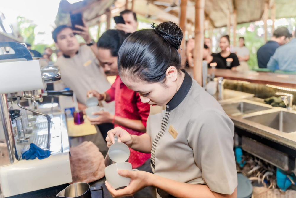 Tongoul pours a latte while another competitor does the same in the background at SPOONS first latte art competition.