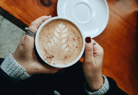 Two hands hold a latte topped with cinnamon.