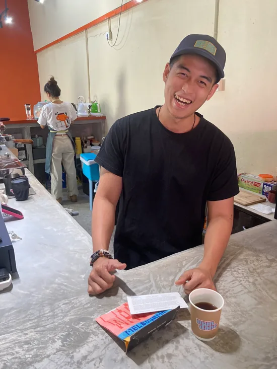 Johny in a photo, caught mid-laugh, as he stands behind the coffee bar.