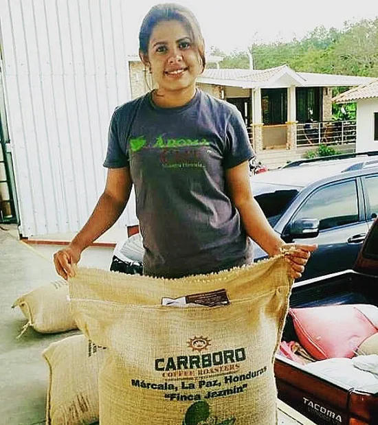 Nancy holds up a large green coffee bag with the logo for carrboro and the words Márcala, La Paz, Honduras, Finca Jazmin.