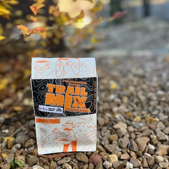 Collab Coffee says Trail Mix: Ethiopian blend from Bibo Coffee and Caffeine Crawl. The bag is white with an orange illustration of a man with mustache picking coffee cherries. 