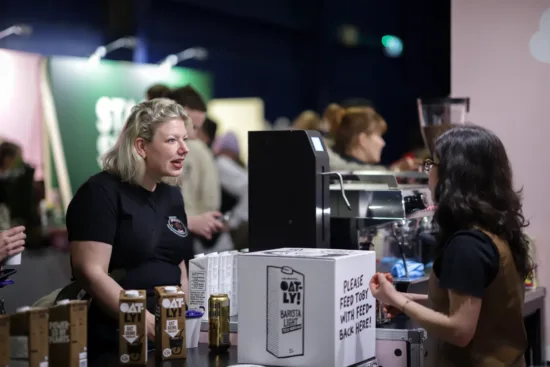 Two people talk at an Oatly oat milk booth.