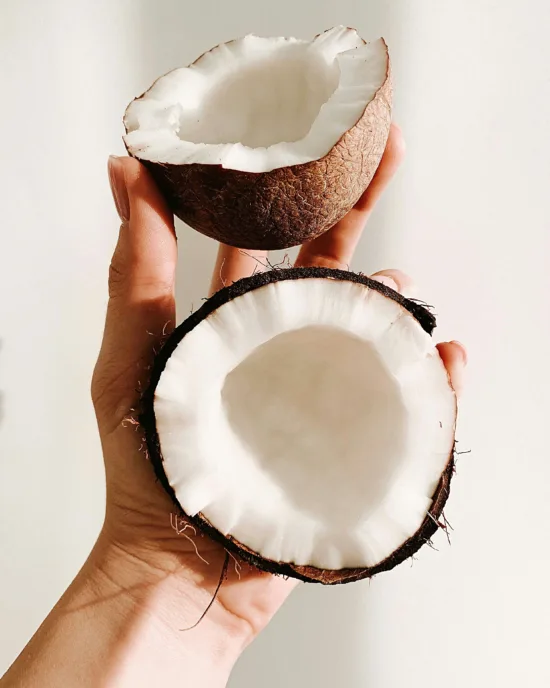 a small coconut in two halves held in a woman's hand.