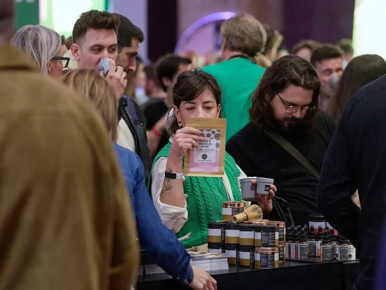 Festival foers look at a table's merchandise, all holding small gray reusable cups from WeCup.