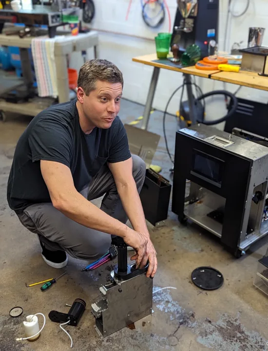 Mike is squatting and the floor and shows the components of the undercounter machine.