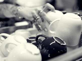 A barista reaches for a mug from a stack of mugs on top of an espresso machine.