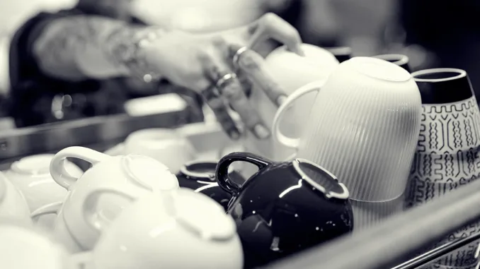 A barista reaches for a mug from a stack of mugs on top of an espresso machine.