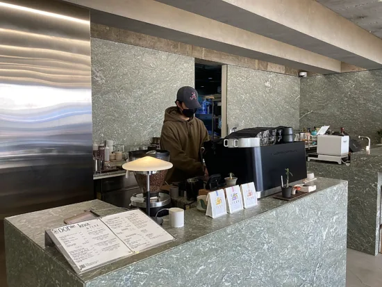 Dorae Knot has gray marble countertops and walls, and a black espresso machine.