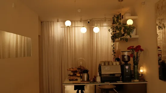 A curtain hangs behind the tiny counter at Calmo, with flowers and pastries on the counter, and cups on top of an espresso machine above the reflective bar.