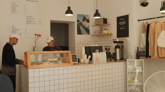 The white interior of ELE ELA with black pendant lights and fixtures, merchandise on the walls and a glass pasrty case.