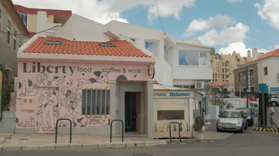 The outside of Liberty, with a tile roof and pink painted outside with a mural of people drinking together.