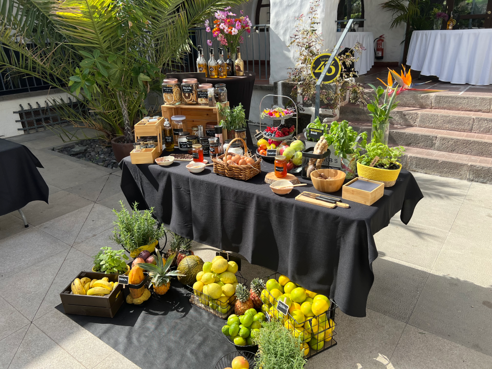 A table decorated with numerous potential ingredients including fruit and alcohol. Additional fruit is stacked in front of the table.